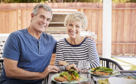 Senior white couple sit at lunch in garden looking to camera